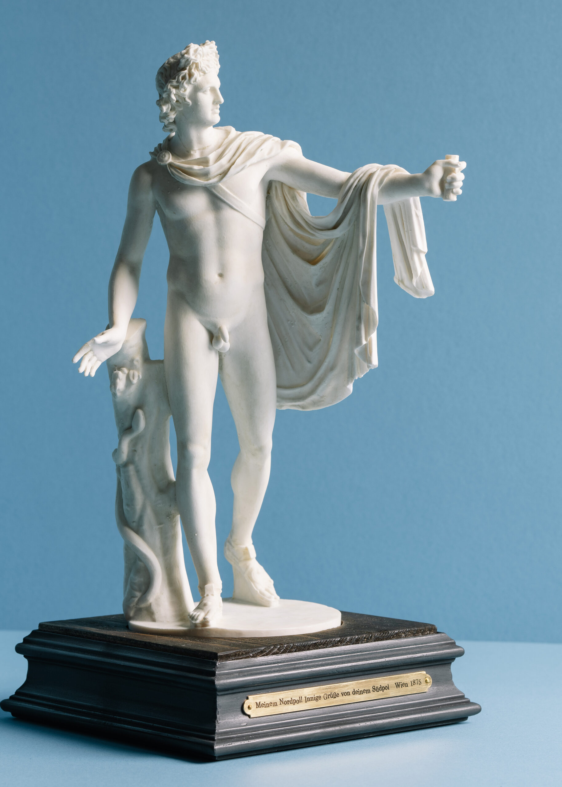 White marble statue of a male figure holding a small object, draped in fabric.