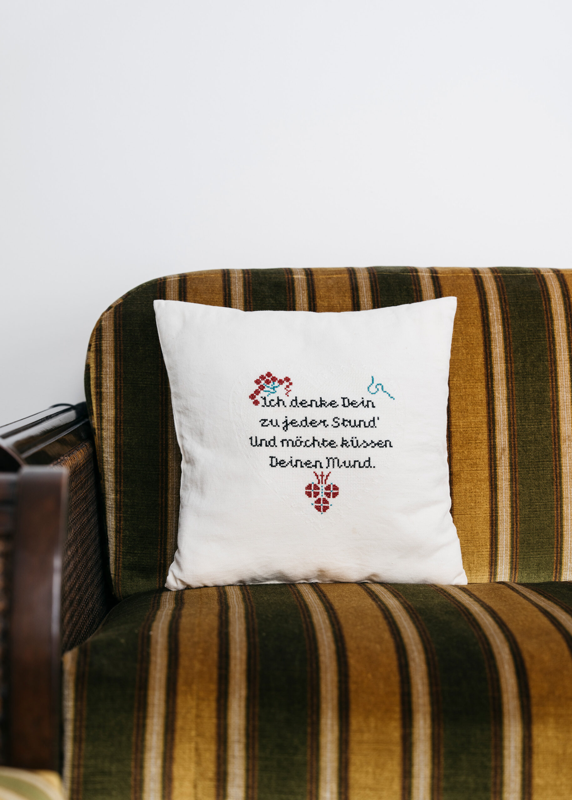 Embroidered pillow on a striped couch with a romantic German phrase.