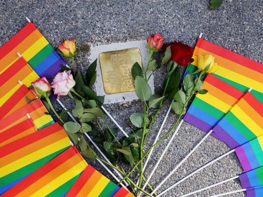 Rainbow flags and roses surround a memorial plaque, honoring LGBTQ+ history and remembrance.