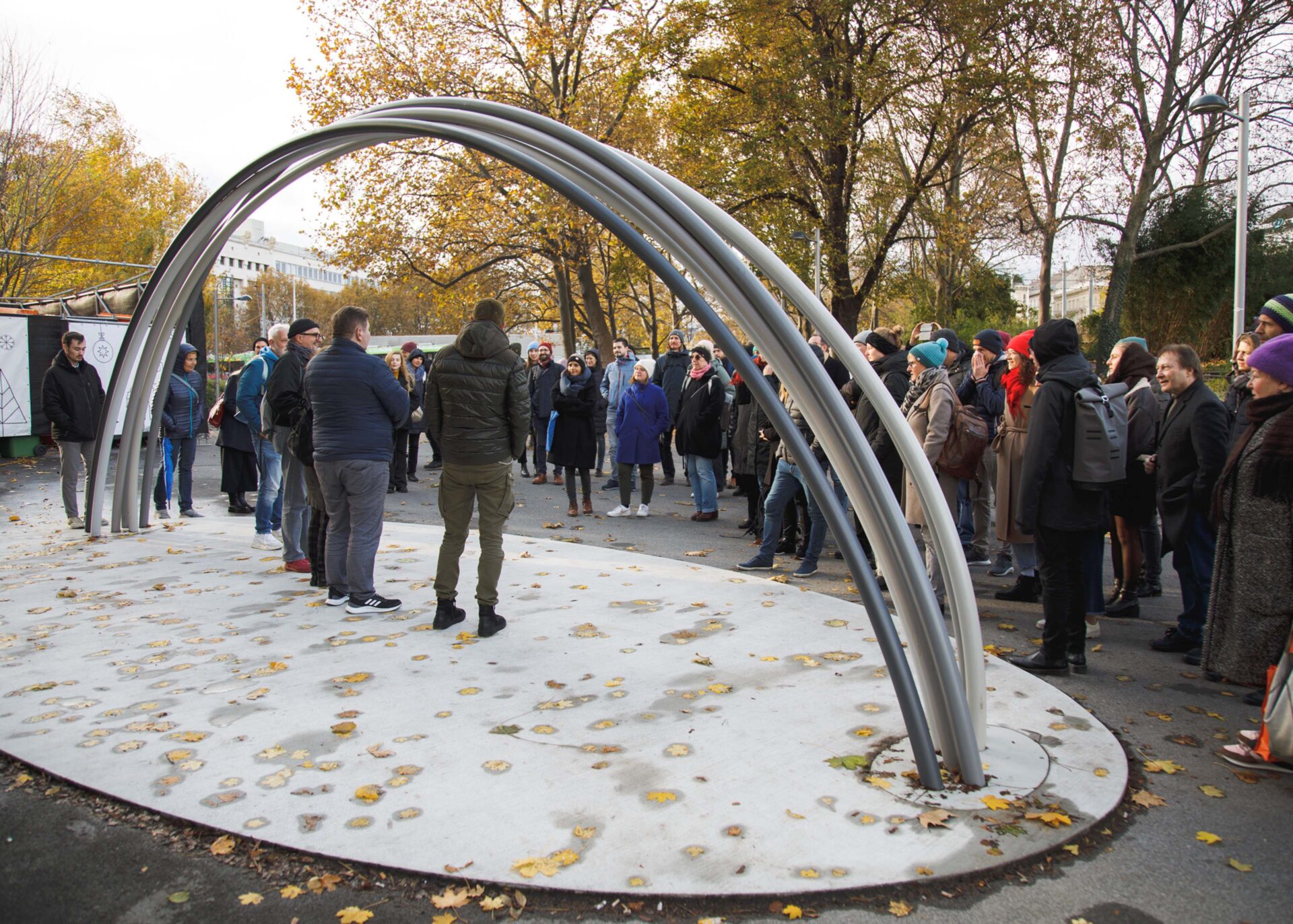 Group of people gathered under a modern arch structure in an outdoor setting.