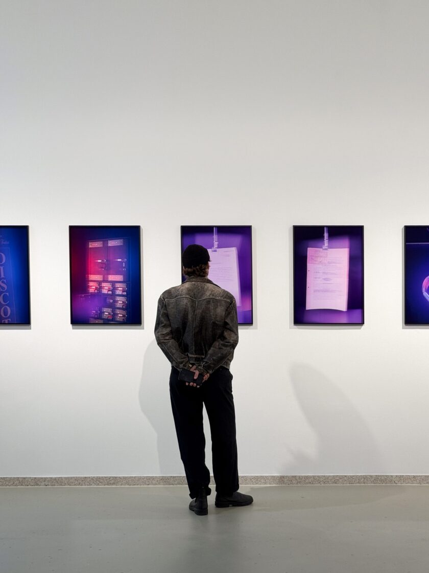 Person betrachtet Kunstwerke von Aura Kiesenhofer in einer Galerie mit bunten Lichtern.