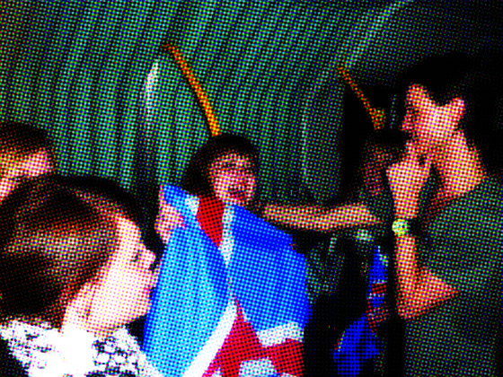 Group celebrating queerness with flags, singing together in a vibrant, energetic atmosphere.
